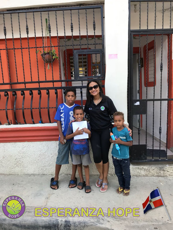 A staff and three boys holding school supplies and toys outside a white and red house