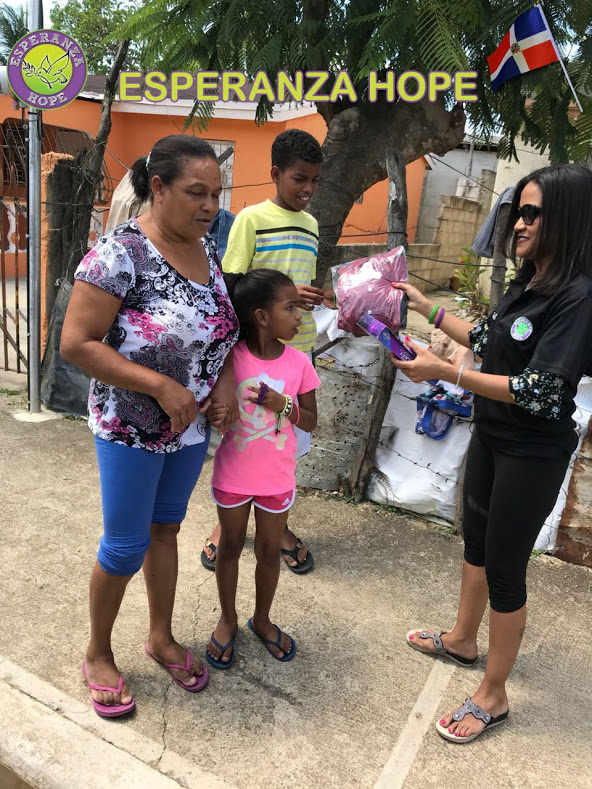 A staff giving away a pack of clothes and a toy to two children with their mother outside