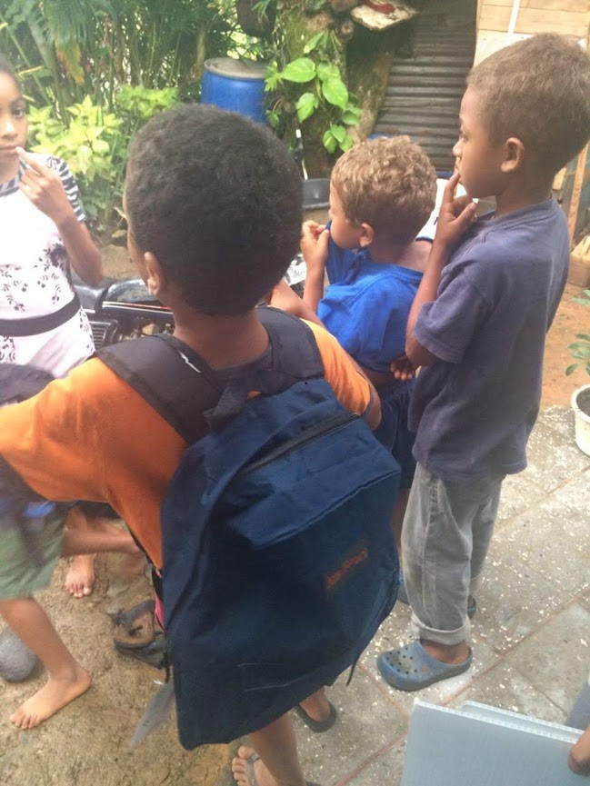 Three boys, one of them already wearing a backpack