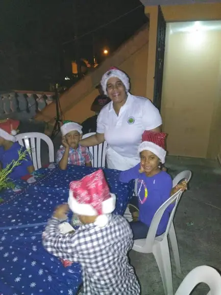 A female staff and children sitting at a table, all wearing Santa hats (night)