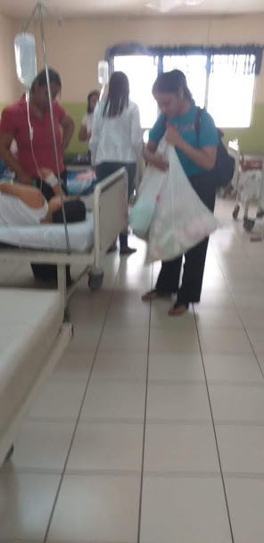 A female staff holding a white plastic bag in front of a hospital bed, blurred