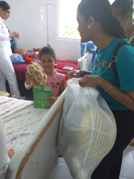 A child smiling and holding a stuffed toy and a book; our staff holding a plastic bag