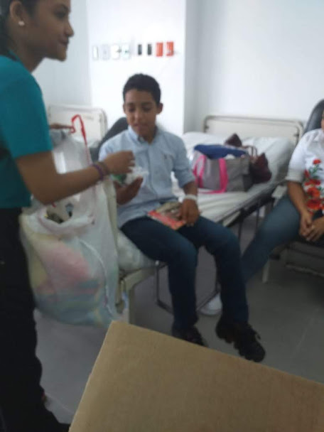 A staff in blue shirt giving a toy to a boy sitting on the hospital bed