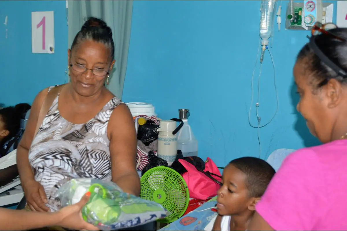 Two women and a child in a hospital bed receiving a pack of clothes