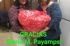 Two women holding a basket wrapped in red cloth and text, “Gracias Maria M. Payamps!”