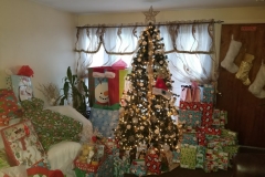 A living room with a Christmas tree that is full of gifts, different angle