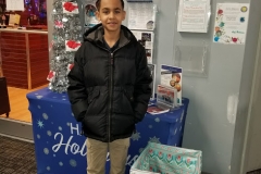 A boy in a jacket in front of a blue Happy Holidays table