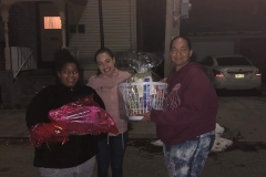 Three women carrying a basket of groceries and a bag of turkey outside a house at night