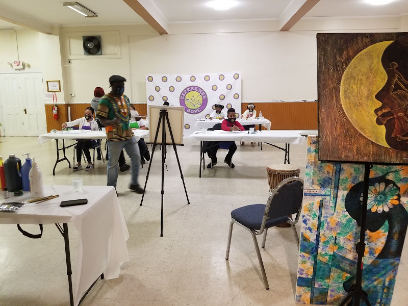 The man in colorful shirt walking toward his canvas in front; attendees continue to paint