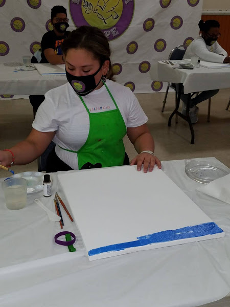 A woman in green apron painting the canvas blue