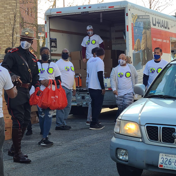 A group of our staff walking, one carrying bstrong bags, a police officer, and an open truck with boxes at the background