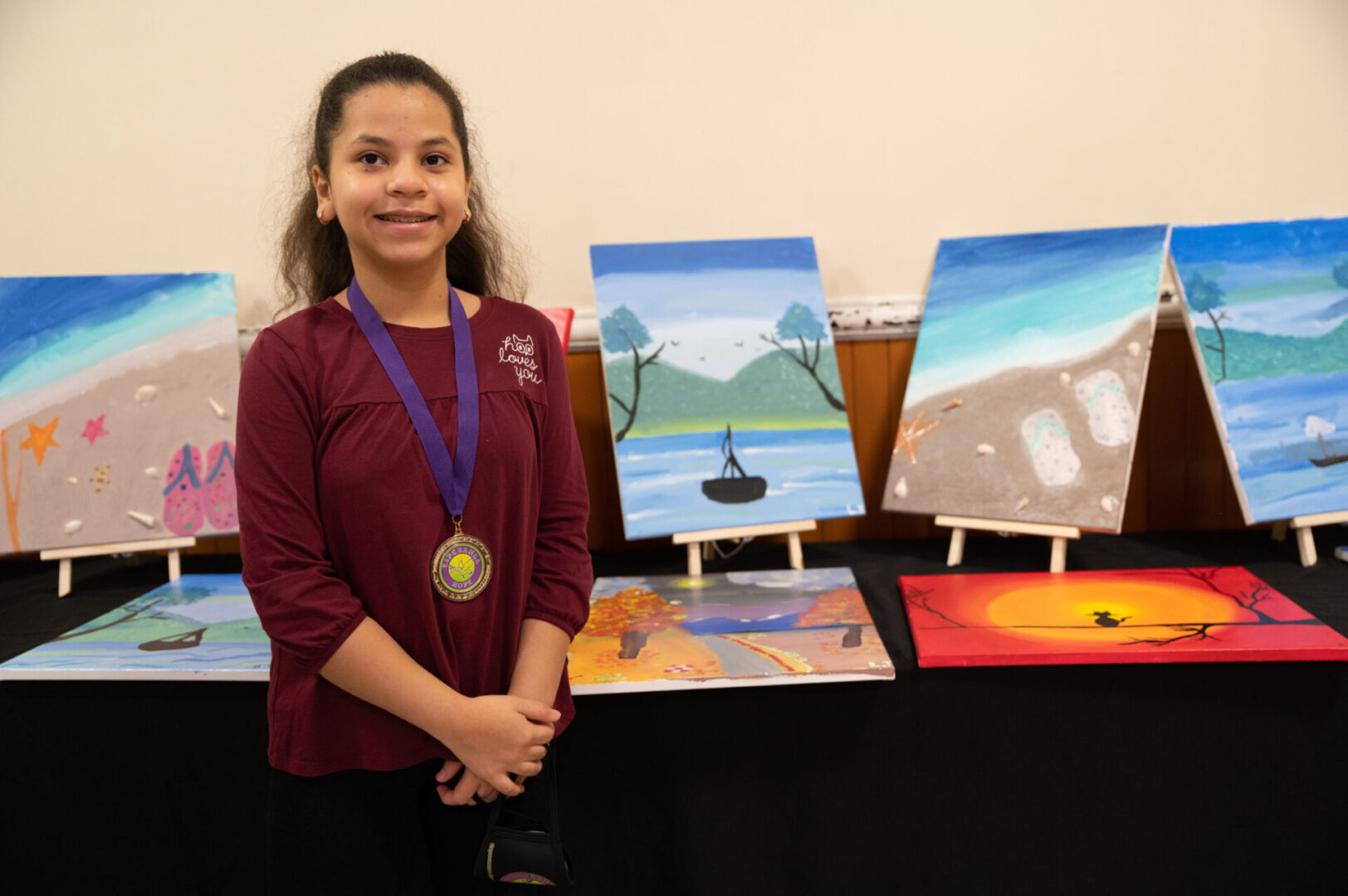 A girl with a medal standing at the table with the paintings