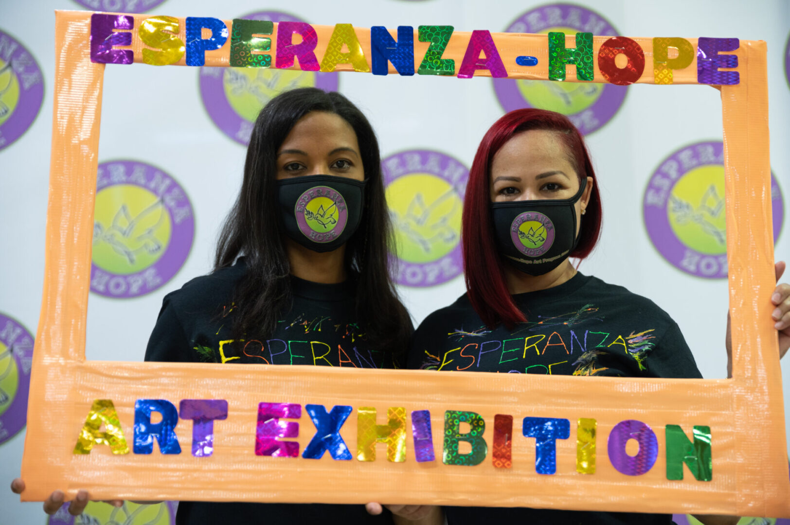 Two of our female staff wearing masks and holding the Esperanza-Hope’s Art Exhibition frame