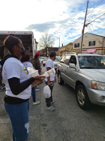 Our staff holds a box of bottled milk and another staff holds a bag of food as cars pass by