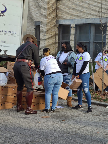 A group of female staff and the church guard getting bags of food from one of the boxes