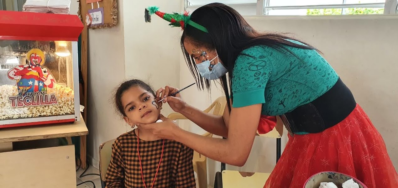Female elf doing face painting on a girl wearing a checkered yellow and black top
