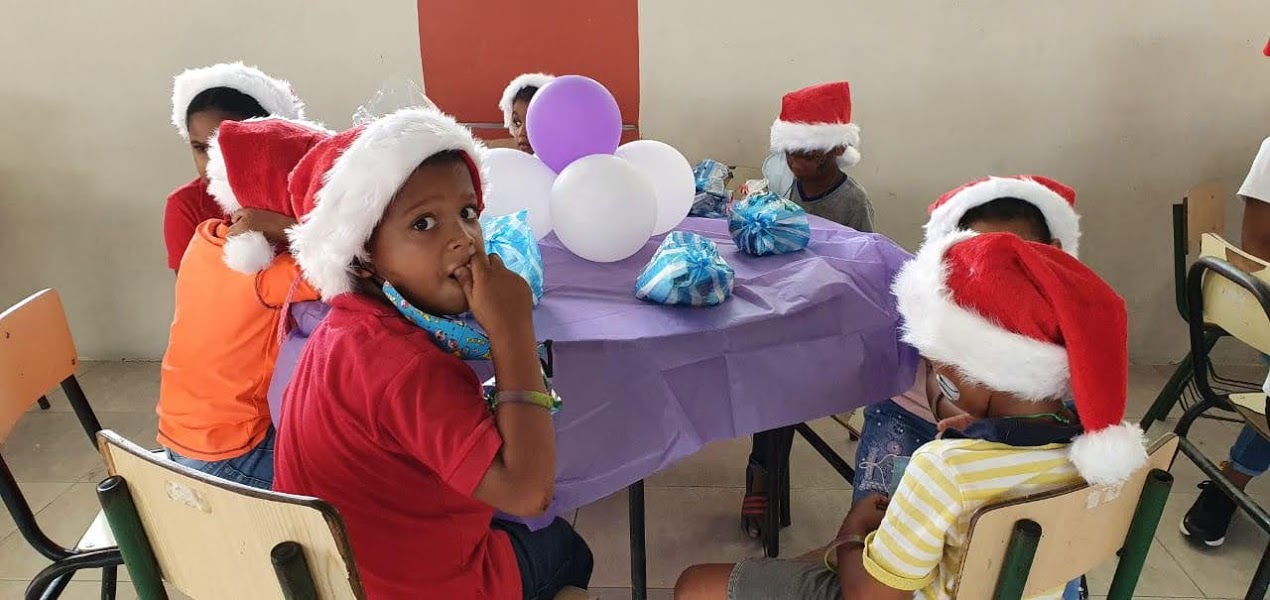 A child wearing a Santa hat and sitting at a table with the others