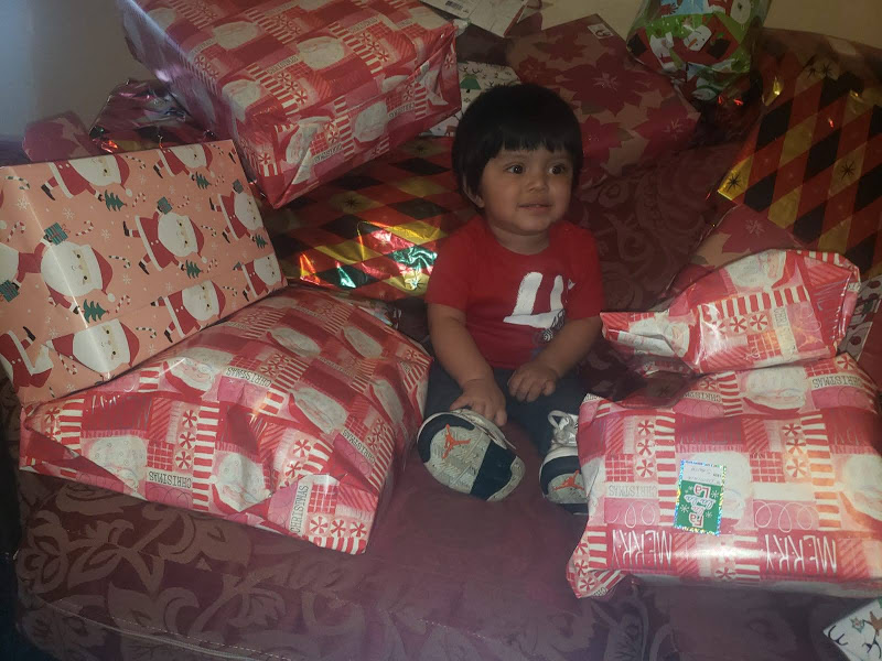 A girl holding a gift and sitting in front of a couch full of Christmas gifts