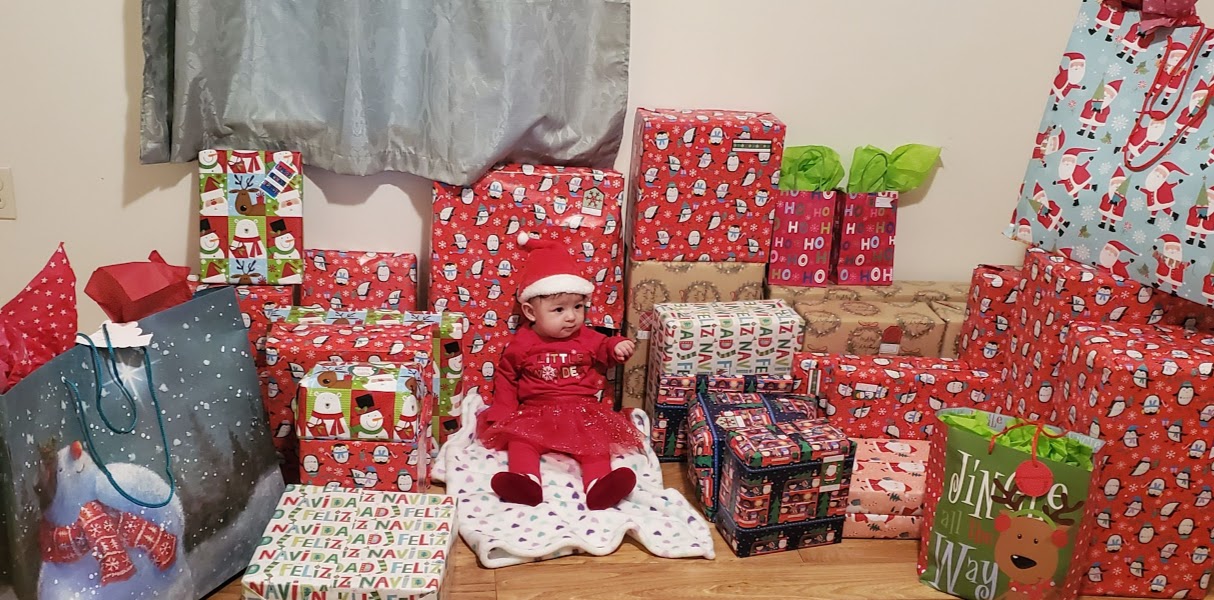 A cute baby wearing a Santa hat with plenty of Christmas gifts around her
