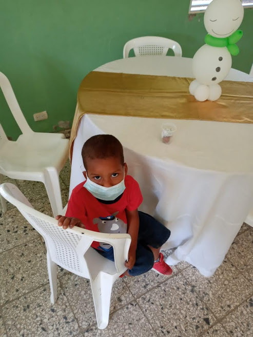 A child wearing a mask sitting alone at a table