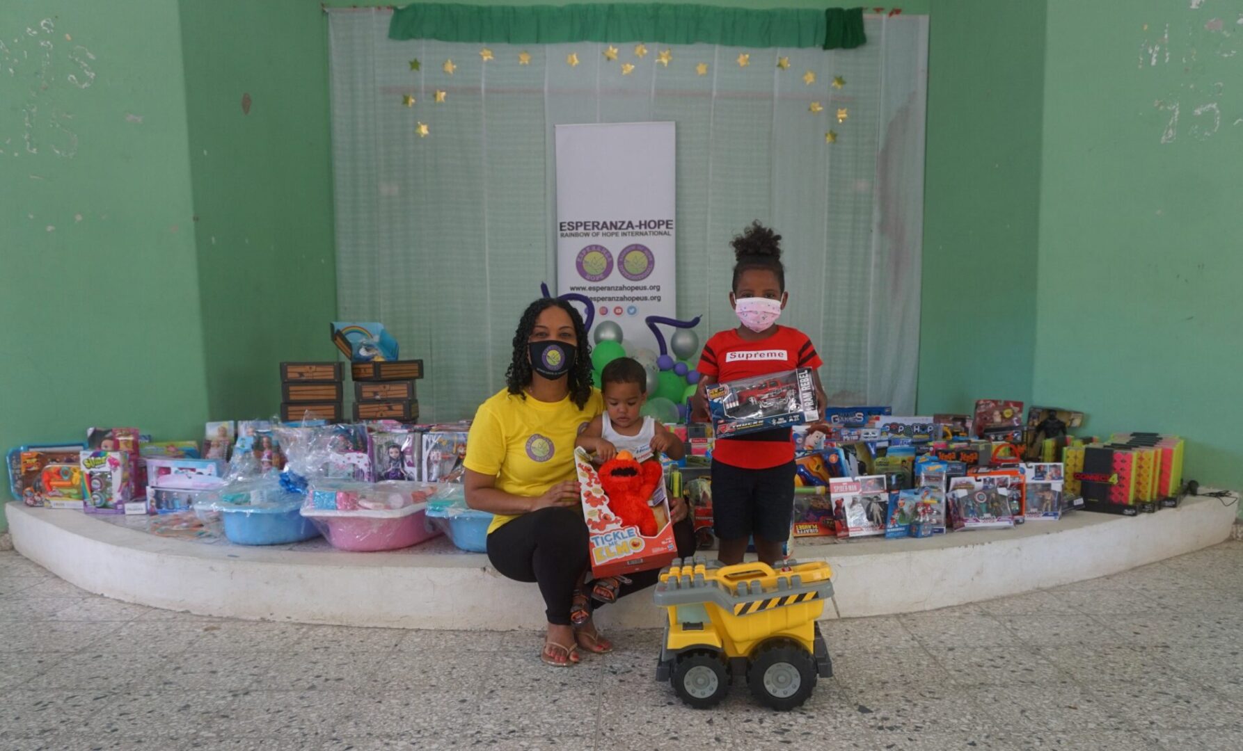 A female staff, a boy with Elmo toy, and another child holding a toy truck