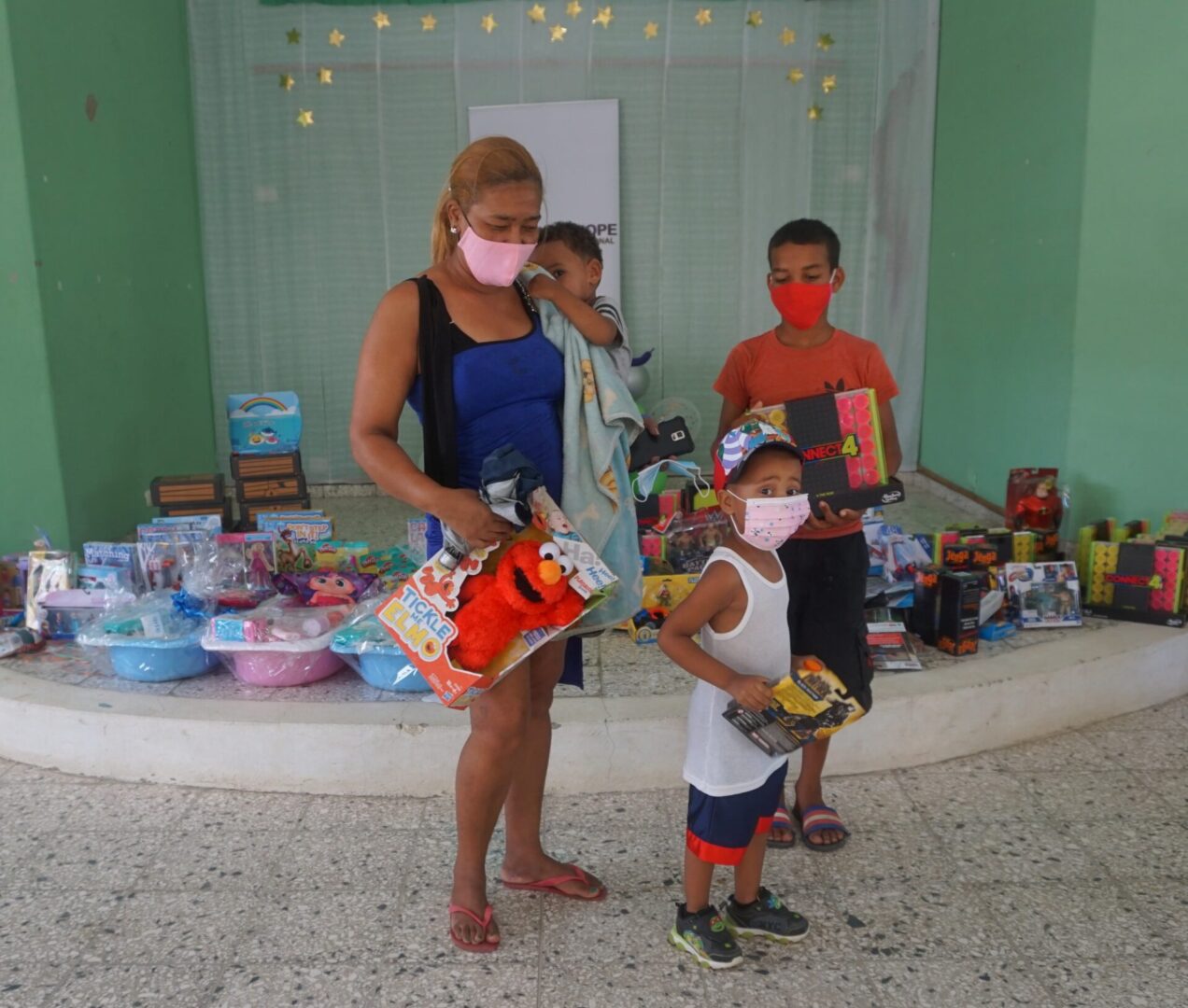 A woman carrying a boy and holding an Elmo toy and two boys holding their toys