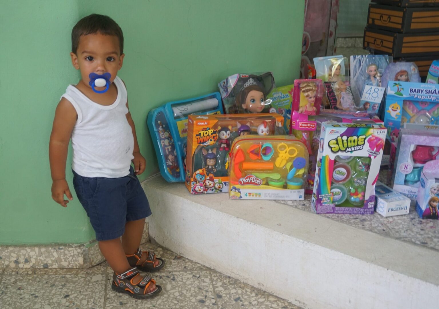 A little boy with a pacifier standing near the platform full of toys
