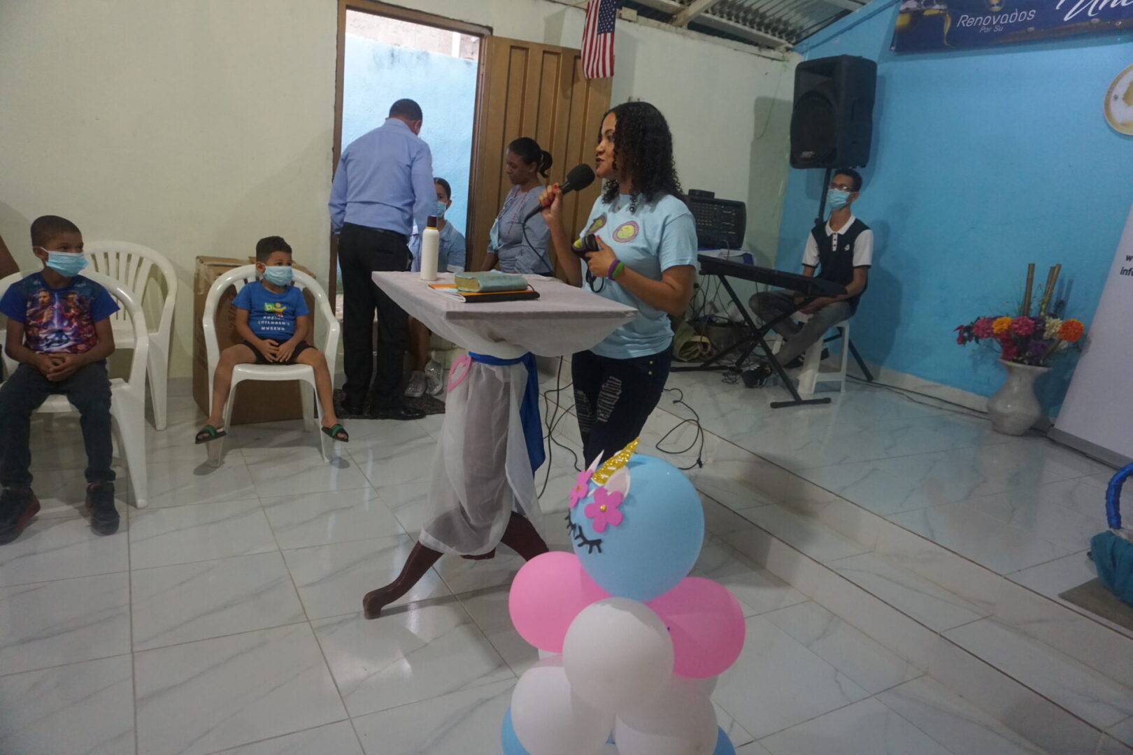 One of our female staff talking in front of the children in the church; other adults talking near the door in front