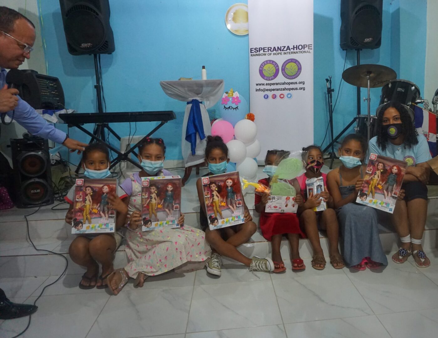 Our staff and six girls sitting near the drum set, each holding a toy