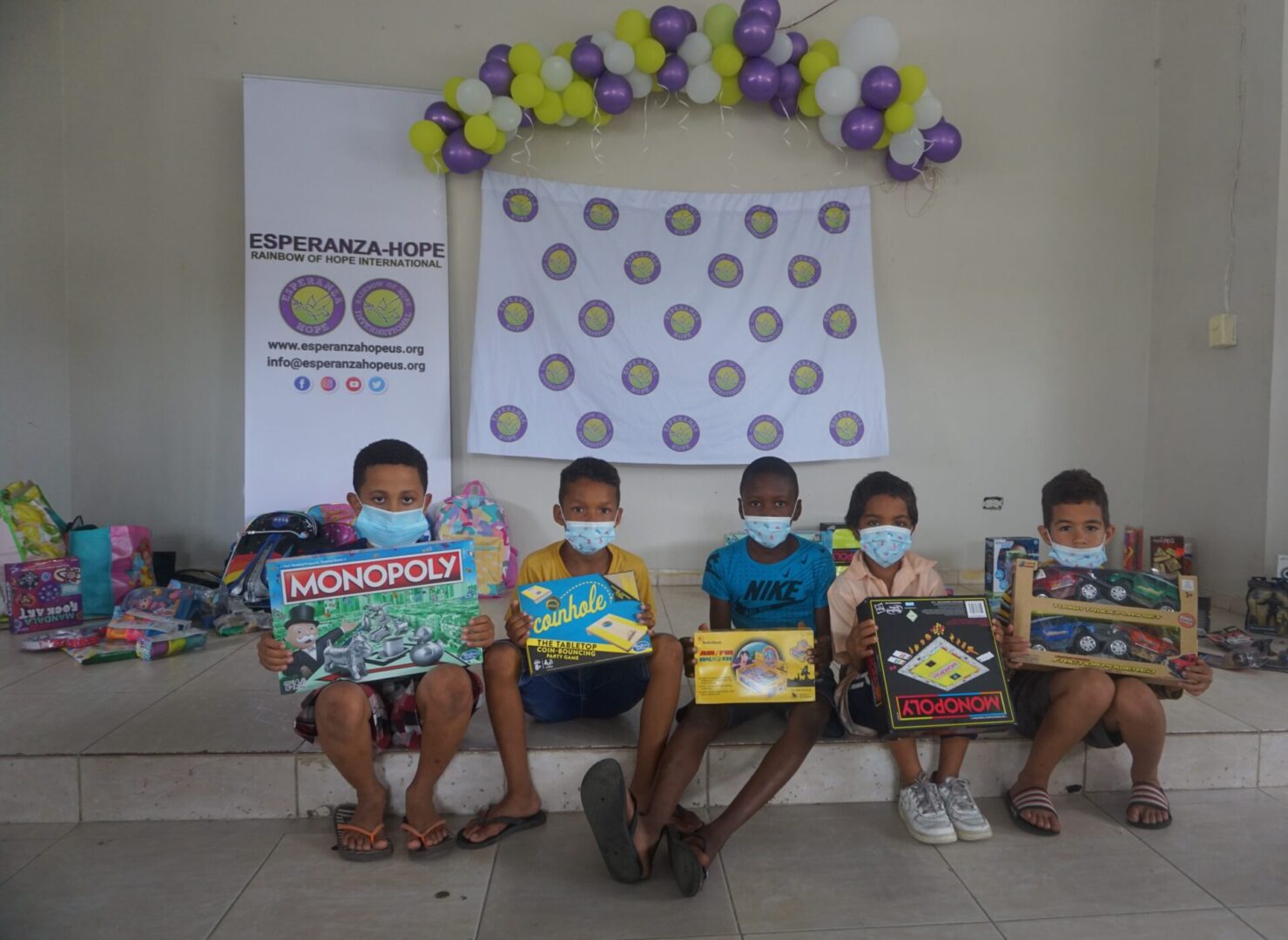 Five boys sitting on the elevated area with balloons and holding boxes of toys