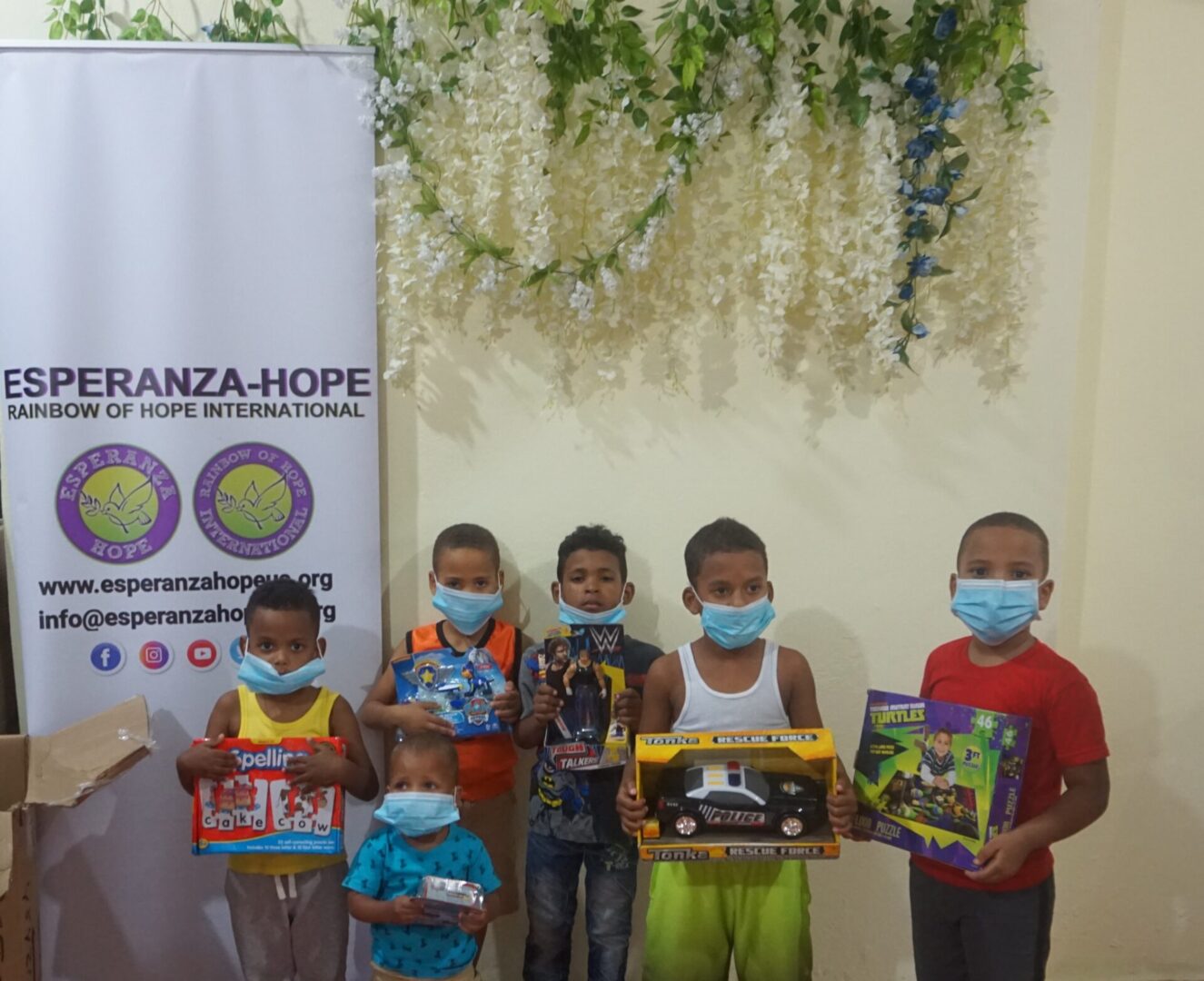 Six young boys holding toys beside the Esperanza-Hope tarpaulin