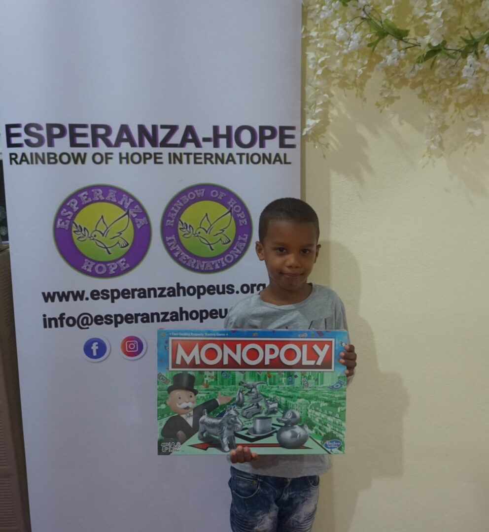 A boy holding a Monopoly box in front of an Esperanza-Hope tarpaulin (version 2)