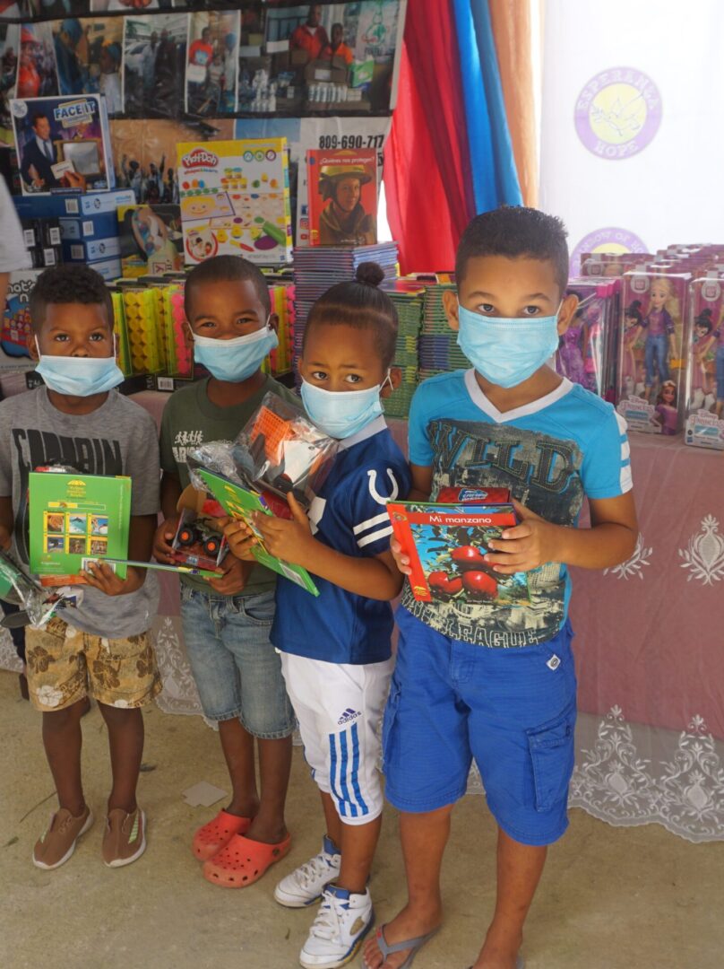 Four boys wearing masks and holding toys in front of a table with books and toys