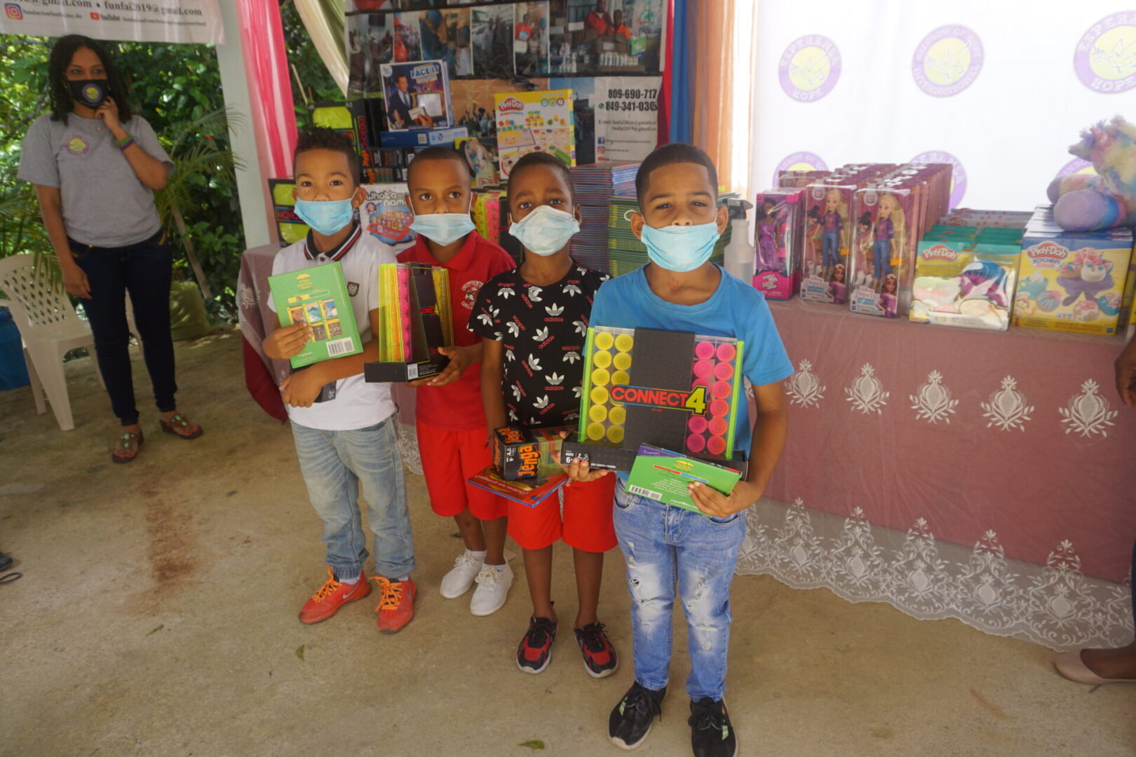 Four boys with masks holding toys in front of a table with books and toys, batch 8