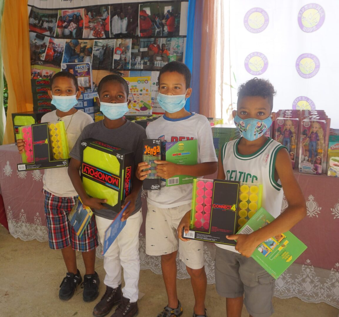 Four boys with masks holding toys in front of a table with books and toys, batch 4