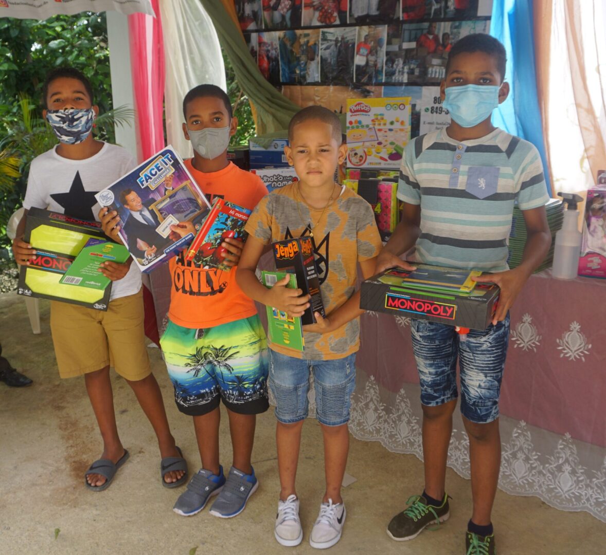 Four boys with masks holding toys in front of a table with books and toys, batch 6