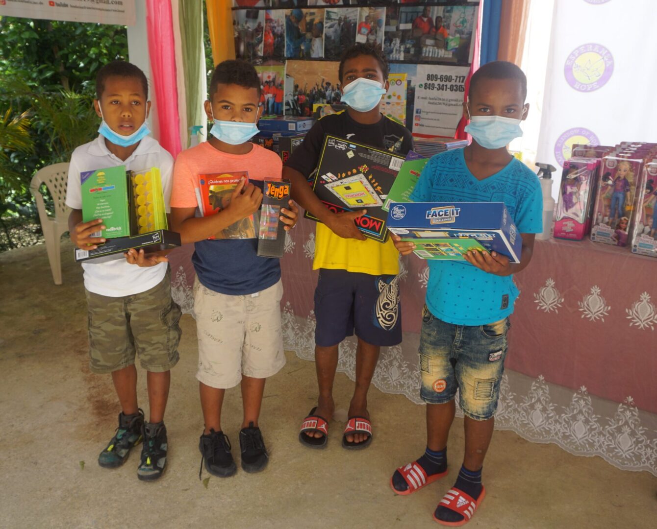 Four boys with masks holding toys in front of a table with books and toys, batch 5