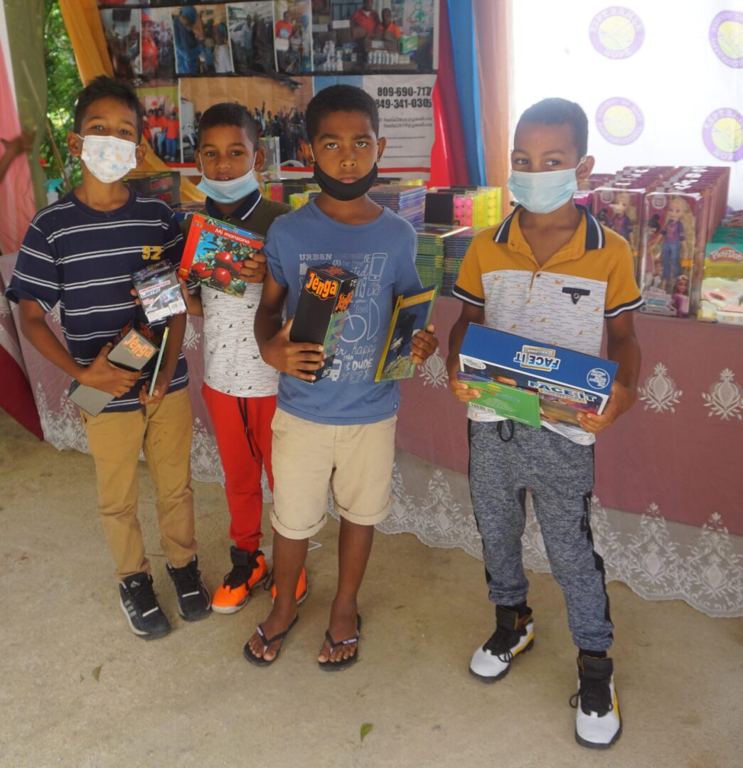 Four boys with masks holding toys in front of a table with books and toys, batch 3