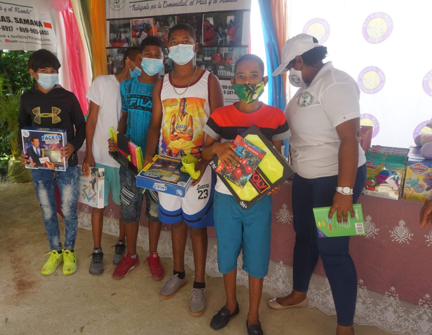 Five older boys holding books and boxes of toys with a staff beside them