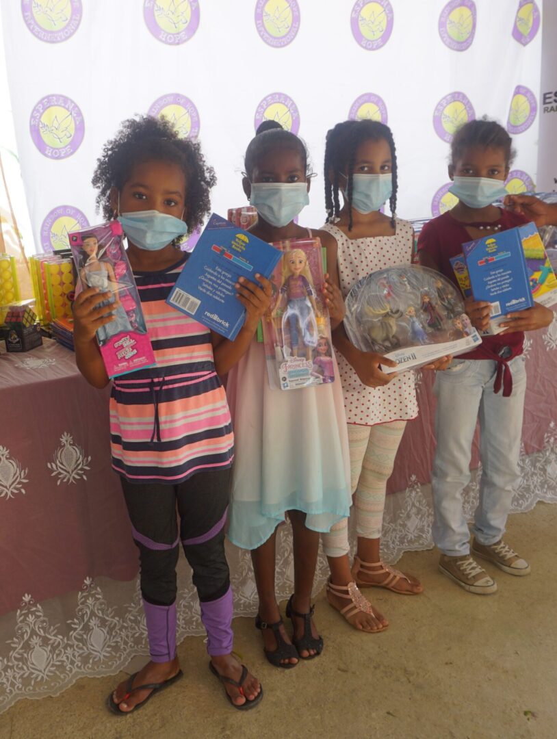Four young girls wearing masks and holding books and toys