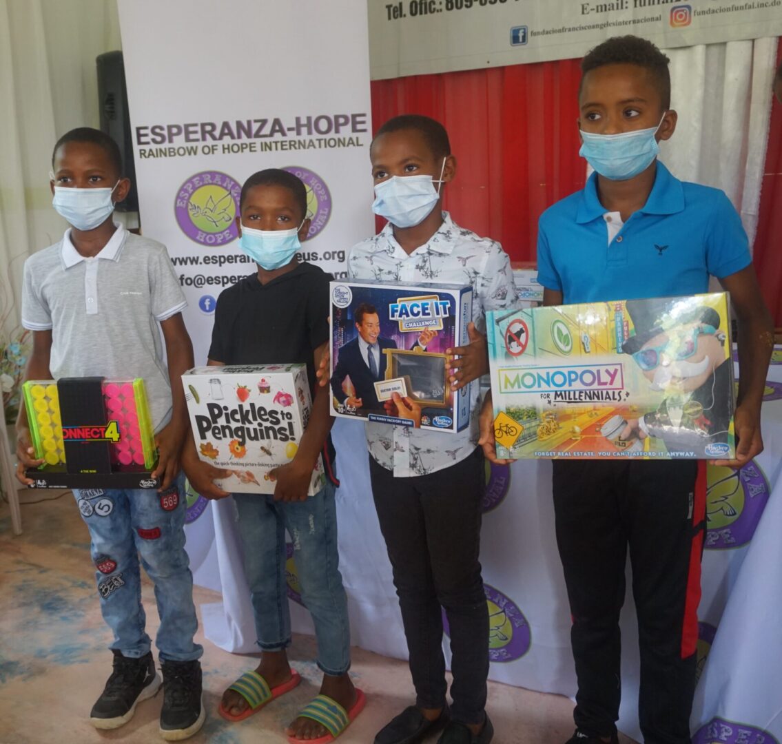 Four boys wearing masks, all holding a board game box