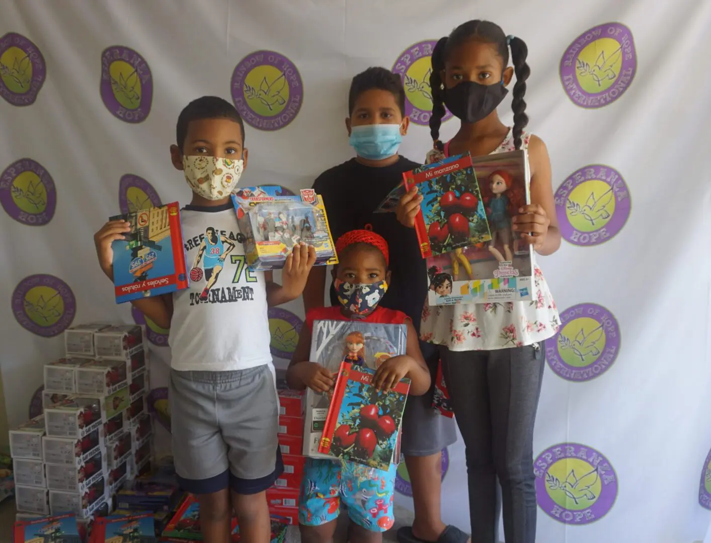 Four children standing against the Esperanza-Hope backdrop with their toys and books, batch 6