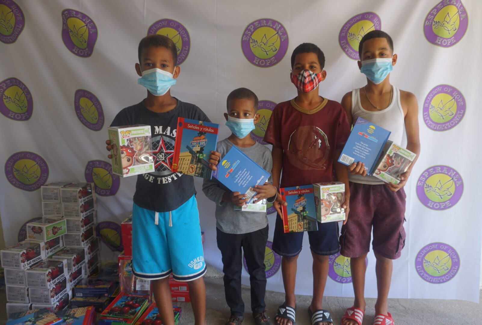 Four boys standing against the Esperanza-Hope backdrop with their toys and books, batch 2