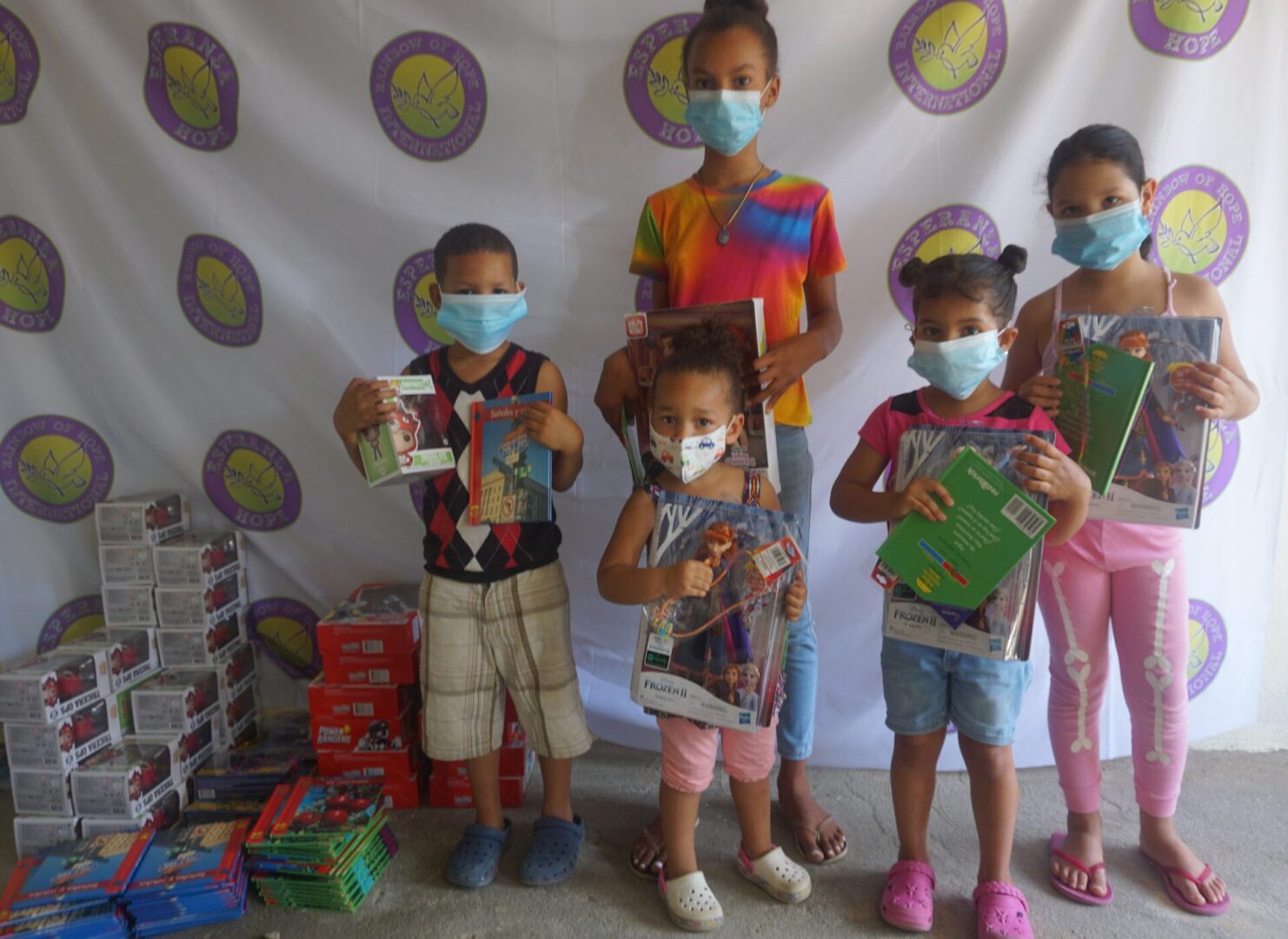 Five children standing against the Esperanza-Hope backdrop with their toys and books, batch 2
