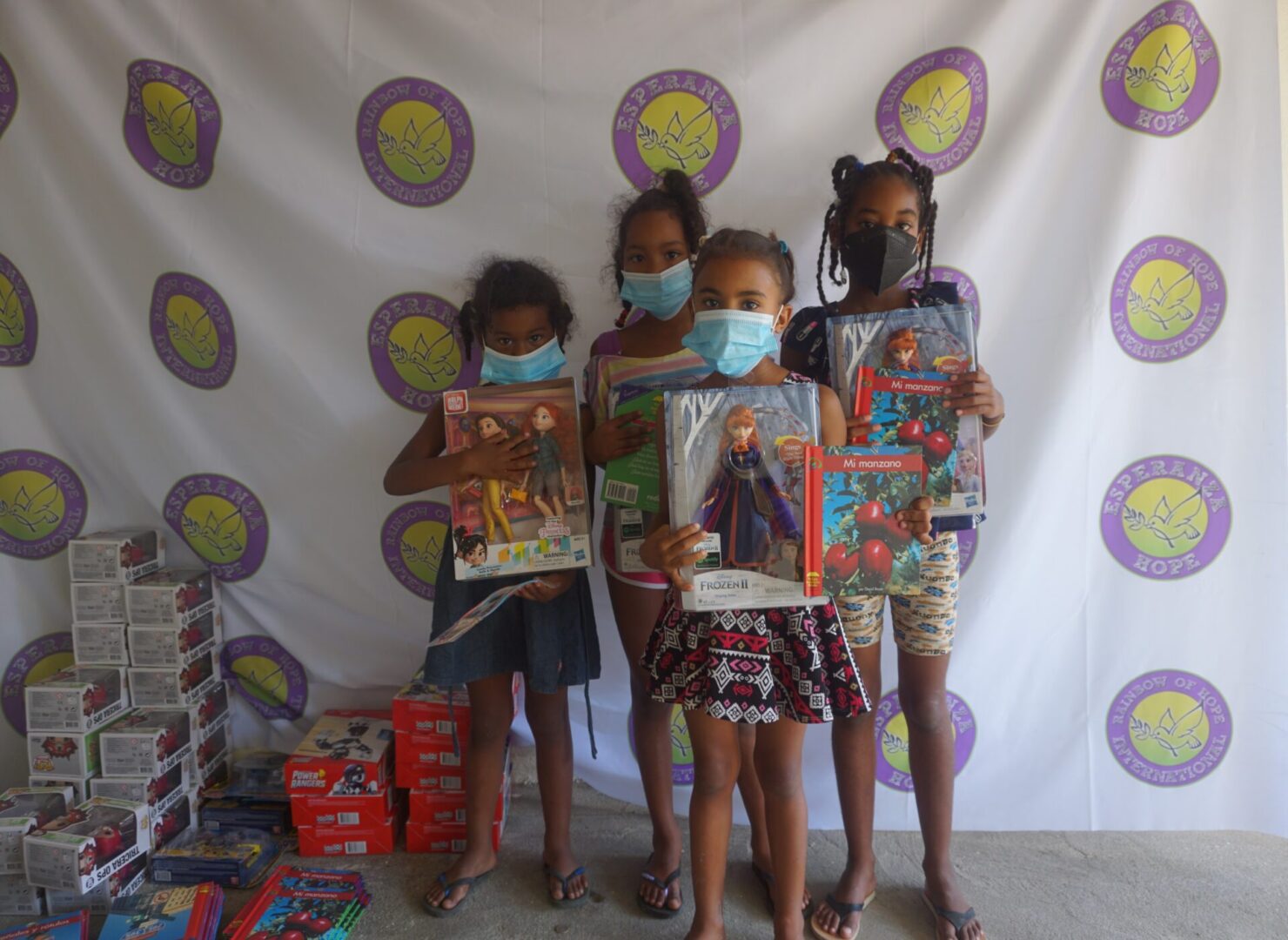 Four girls standing against the Esperanza-Hope backdrop with their toys and books