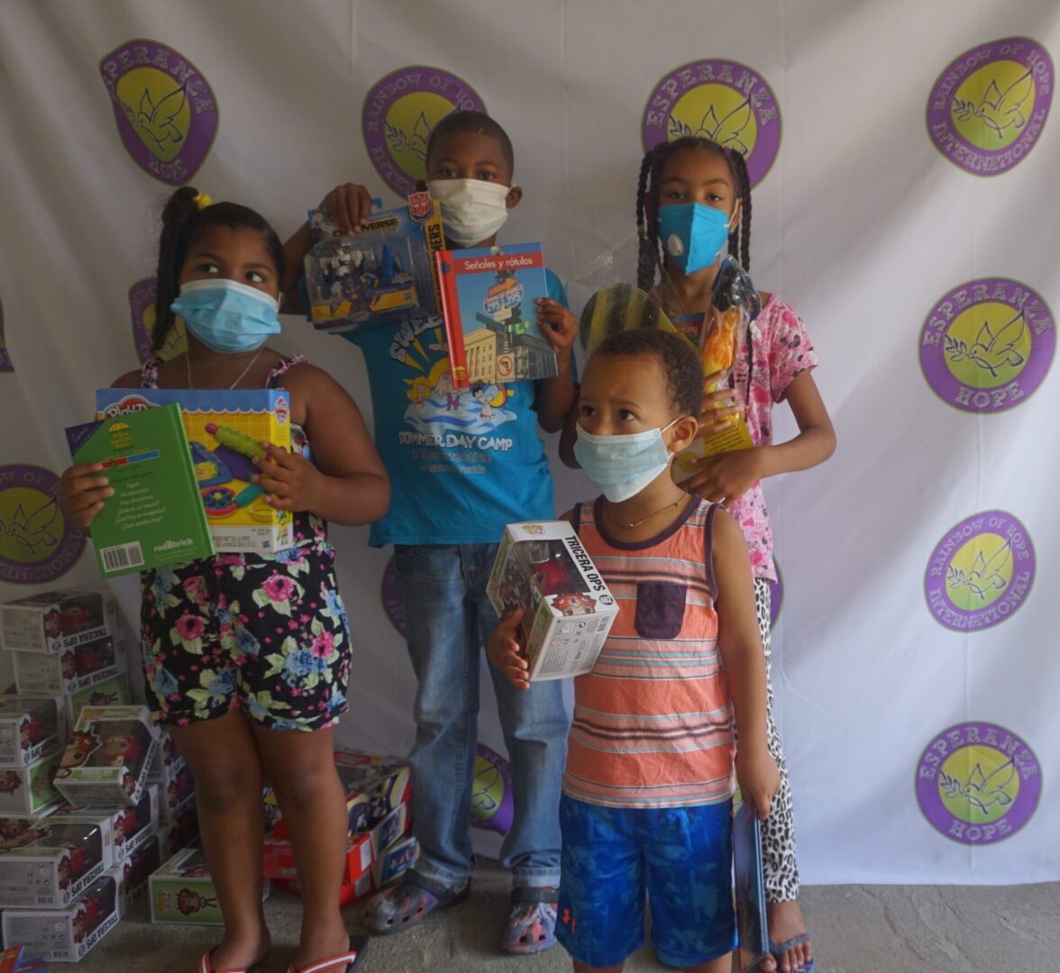 Four children standing against the Esperanza-Hope backdrop with their toys and books