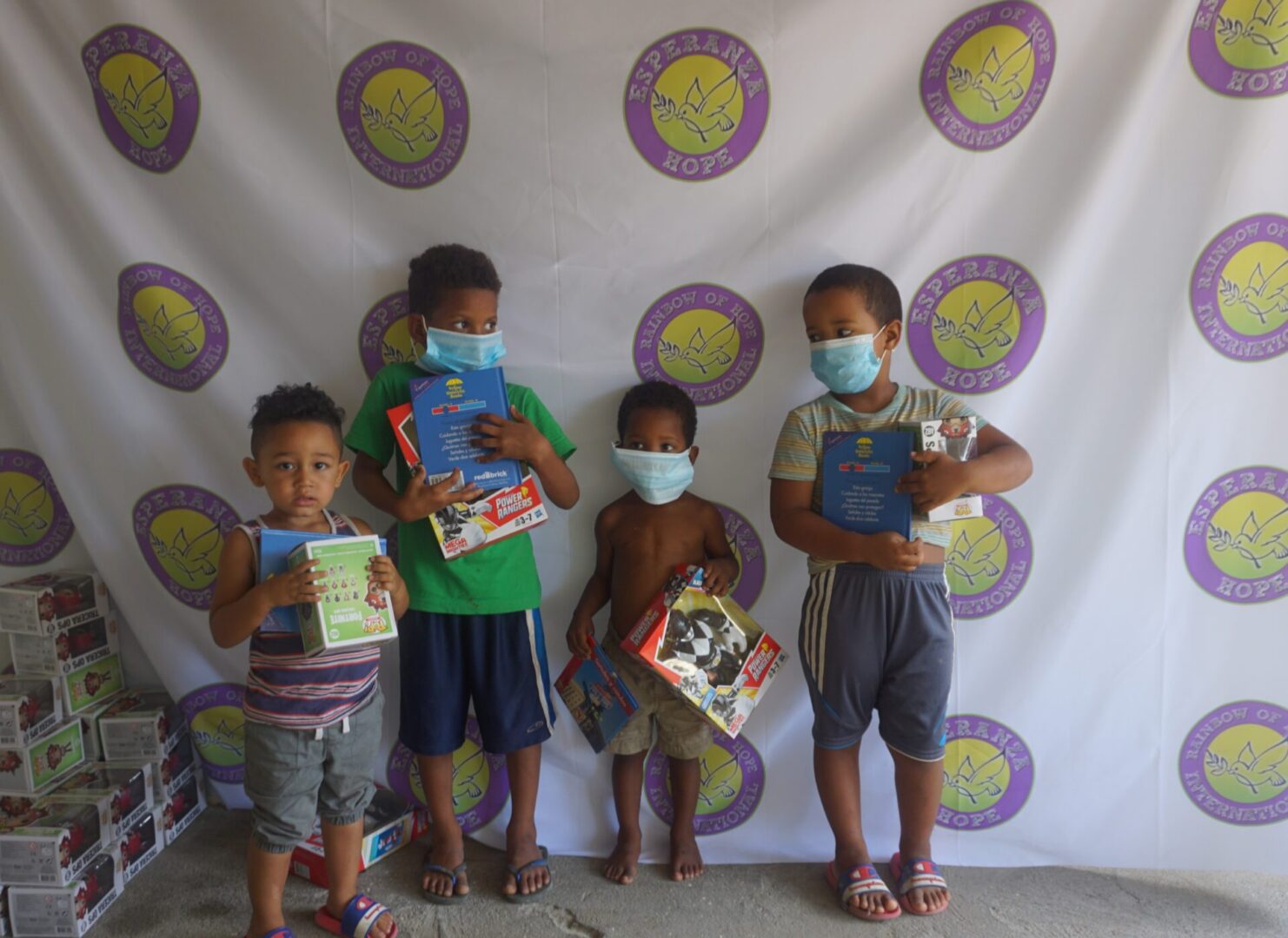 Four young boys standing against the Esperanza-Hope backdrop with their toys and books