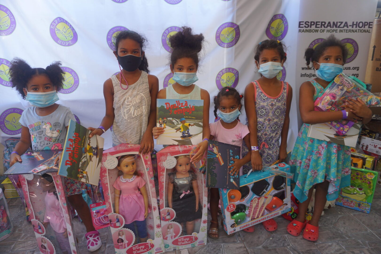 Six girls standing against the Esperanza-Hope backdrop with their toys and books, batch 2