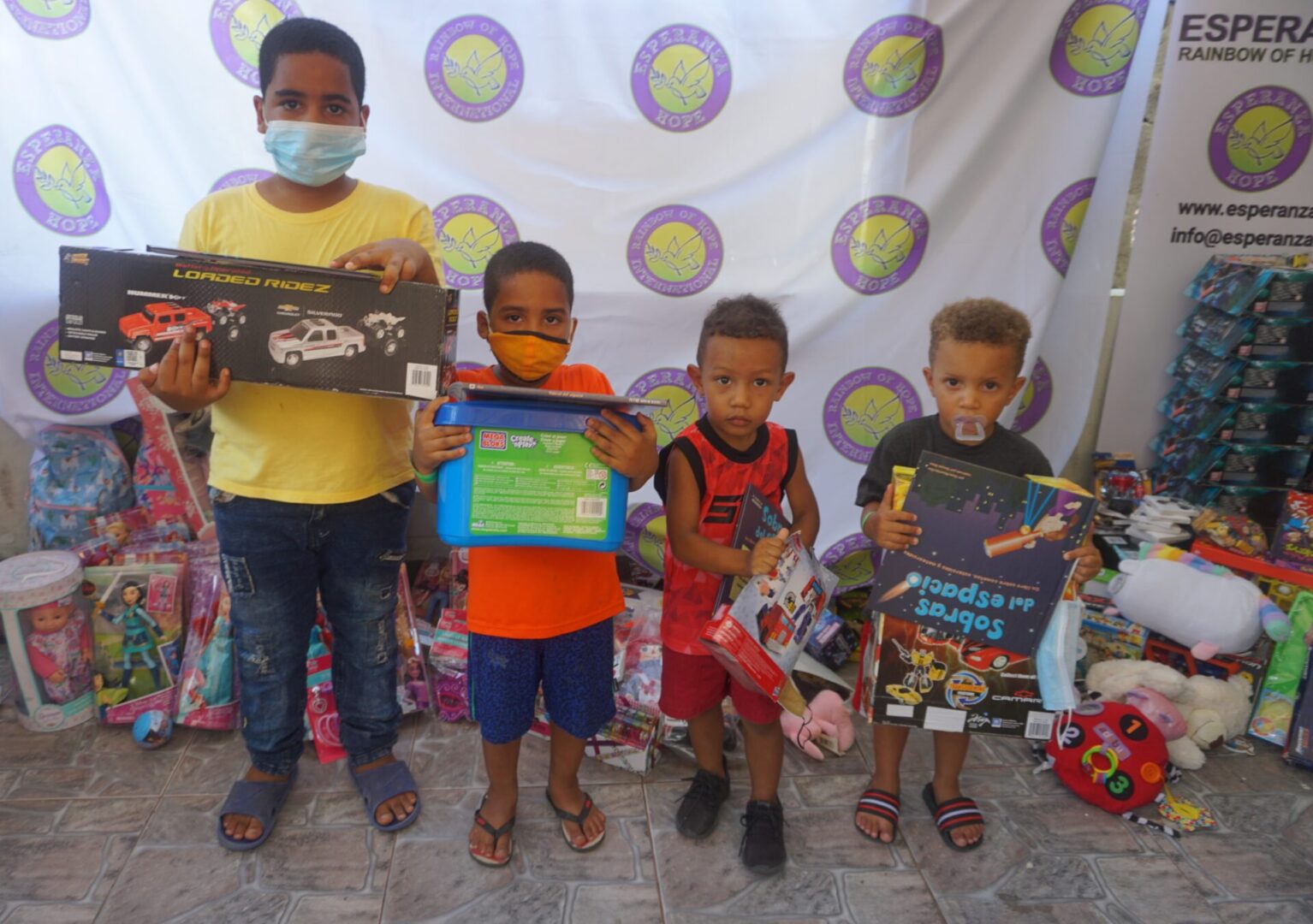 Four boys standing against the Esperanza-Hope backdrop with their toys and books, batch 3