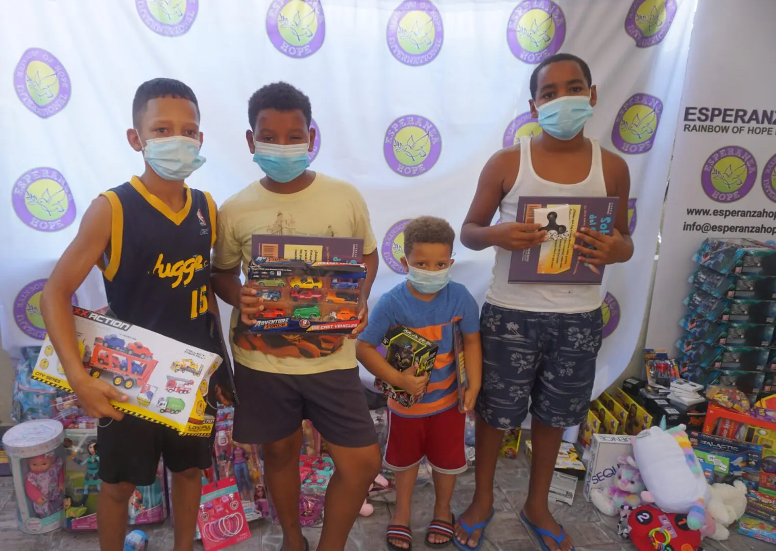 Four boys standing against the Esperanza-Hope backdrop with their toys and books, batch 4